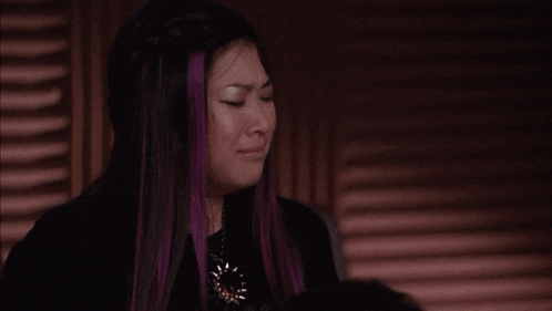 a woman with purple hair is crying while wearing a black shirt and a necklace .