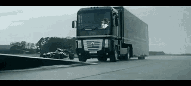 a large black truck is driving down a road next to a race car .