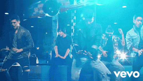 a group of men are dancing in front of a sign that says vevo on it