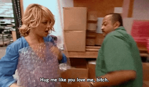 a woman is talking to a man in a warehouse and says " hug me like you love me bitch " .