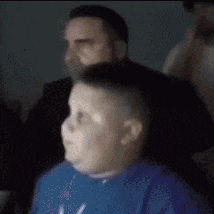 a boy in a blue shirt is sitting in front of a man .