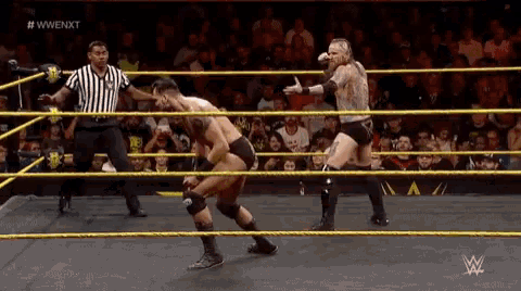 two men are wrestling in a wrestling ring with a referee standing behind them .