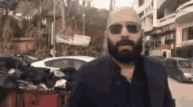 a bald man with a beard and sunglasses is standing in front of a pile of trash .