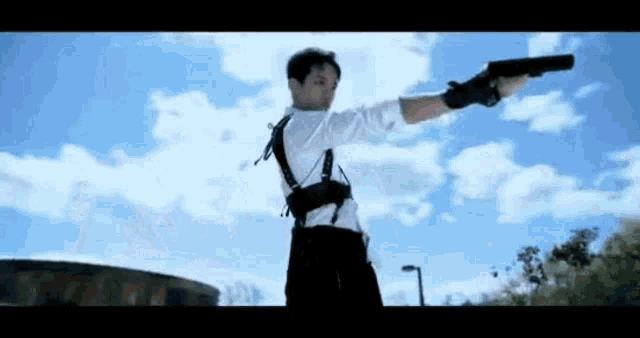 a man in a white shirt and black pants is holding a gun in the air .