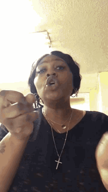 a woman wearing a black shirt and a cross necklace is making a funny face .