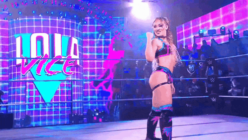 a female wrestler is standing in a wrestling ring in front of a large screen .