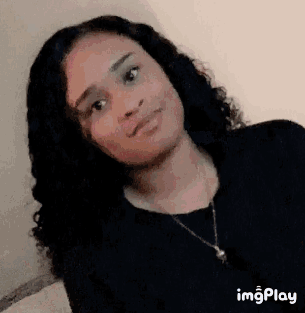 a girl with curly hair is wearing a black shirt and a necklace .