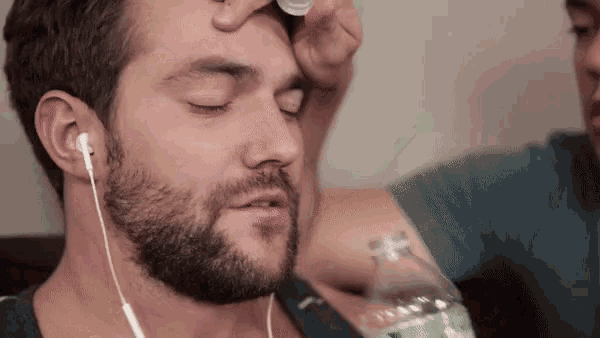 a man with a beard and ear buds is holding a bottle of water on his forehead