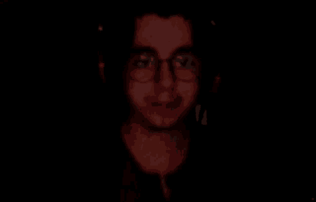 a close up of a man wearing glasses in the dark .
