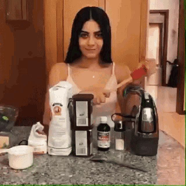 a woman in a white tank top is standing in front of a counter holding a blender and a box of pringles .