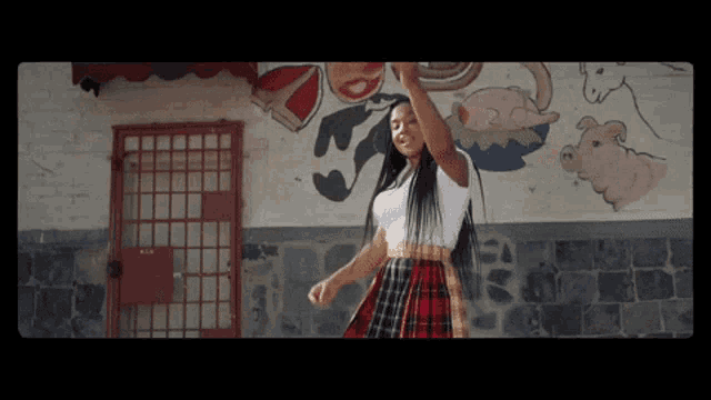 a woman in a plaid skirt is dancing in front of a wall with drawings on it