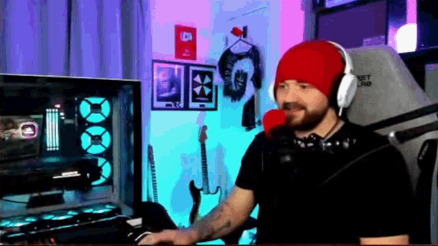 a man wearing headphones and a red hat is sitting at a desk in front of a computer .