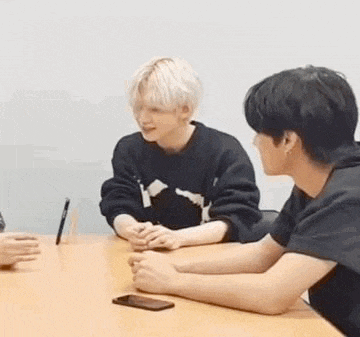 a couple of men are sitting at a table with a cell phone .