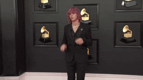 a man in a suit is standing in front of a wall with grammy trophies on it .