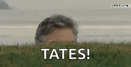 a man is peeking out from behind a lush green field and says tates !