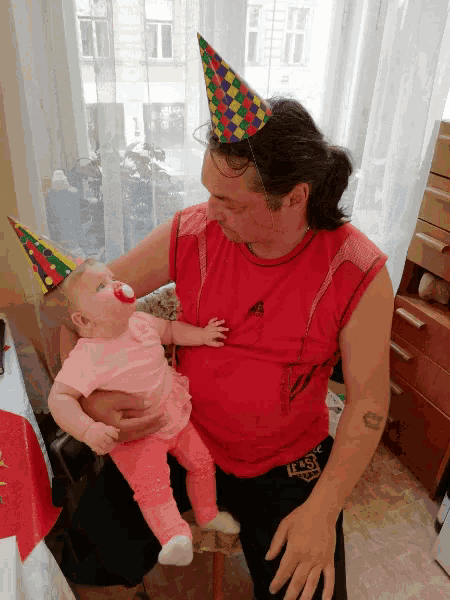 a man wearing a party hat is holding a baby in his arms