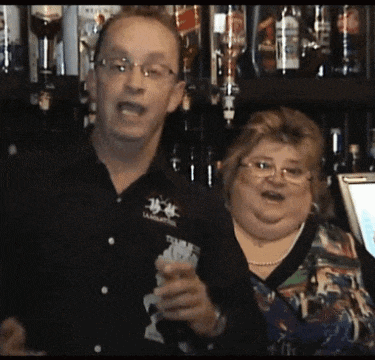 a man and a woman are standing in front of a bar with bottles of alcohol