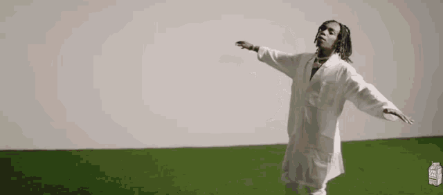 a man in a white coat is standing in a field of grass with his arms outstretched .