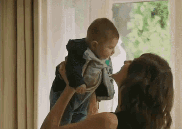 a woman is holding a baby in her arms in front of a window