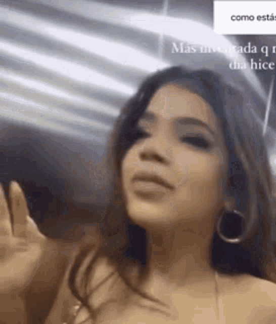 a woman wearing hoop earrings is waving her hand in a video