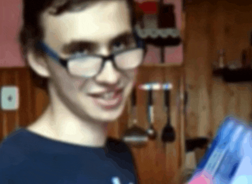 a young man wearing glasses and a blue shirt is holding a blue box .
