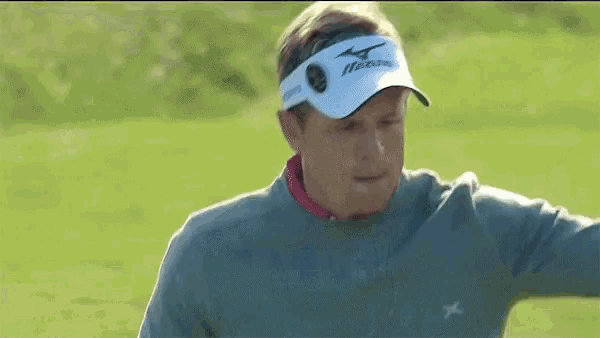 a man wearing a gray sweater and a white hat is standing on a golf course .