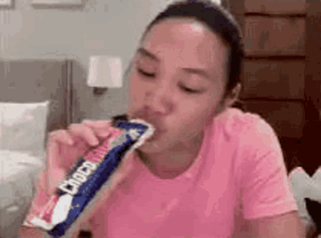 a woman in a pink shirt is eating a bar of chocolate .