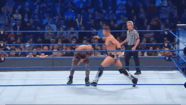 two men are wrestling in a wrestling ring with a referee standing between them .