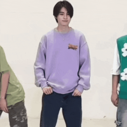 a young man wearing a purple sweatshirt is standing next to two other young men .