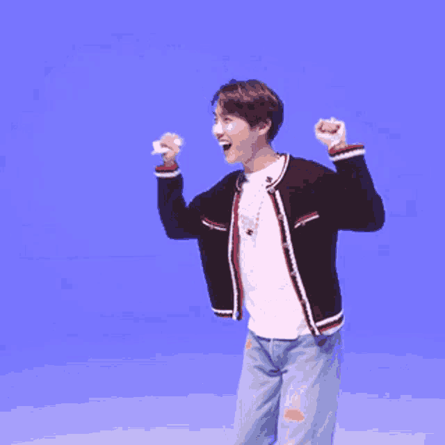 a young man in a black jacket and white shirt is standing in front of a blue background with his arms in the air