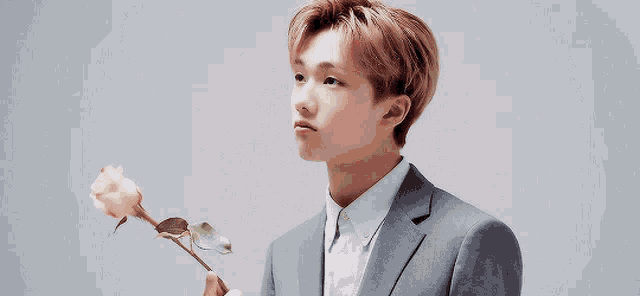 a young man in a suit is holding a single rose