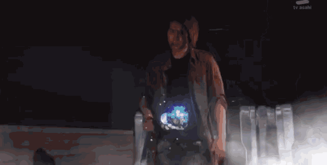 a man is standing in a dark room with a tv asahi logo on the bottom right