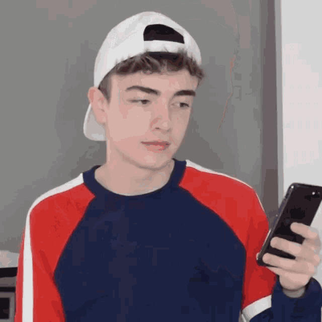 a young man wearing a baseball cap and a sweater is looking at his phone