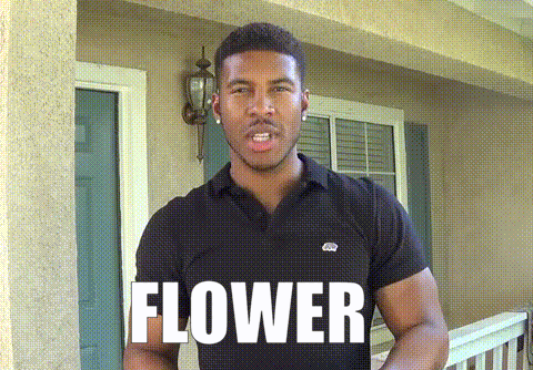 a man in a black shirt is standing in front of a house and the word flower is on the front of his shirt