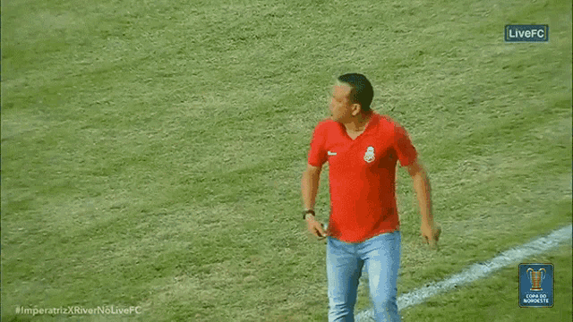 a man in a red shirt is walking on a soccer field in front of a live fc banner