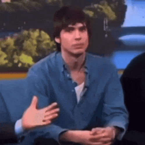 a man in a blue shirt is sitting on a couch and talking .