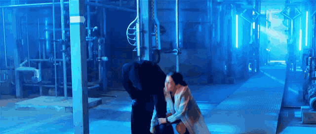 a woman is kneeling down next to a man in a dark room with blue lights .