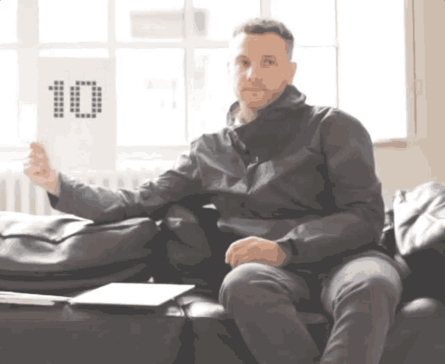 a man sits on a couch holding up a sign that says 10