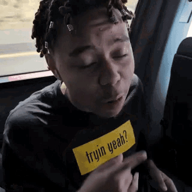 a man wearing a shirt that says tryin yeah is sitting in the back seat of a car .