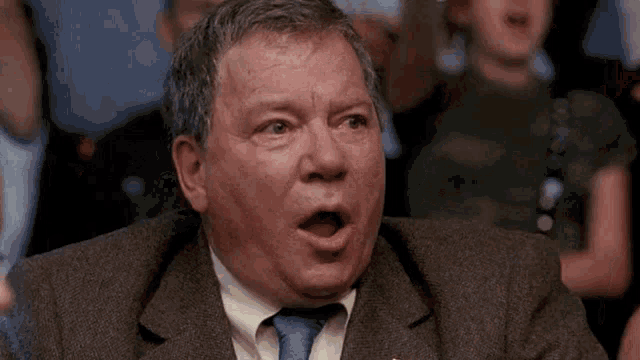 a man in a suit and tie is making a surprised face with his mouth open .