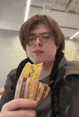 a man wearing glasses is eating a sandwich from a bag .
