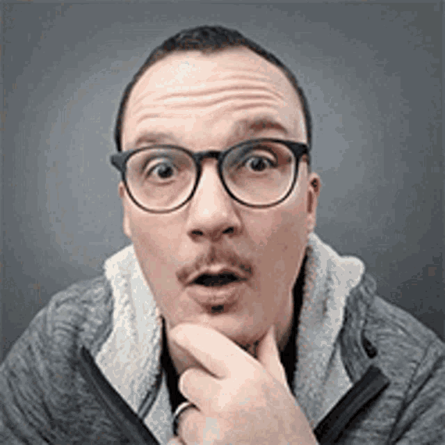 a man wearing glasses and a jacket is making a surprised face .
