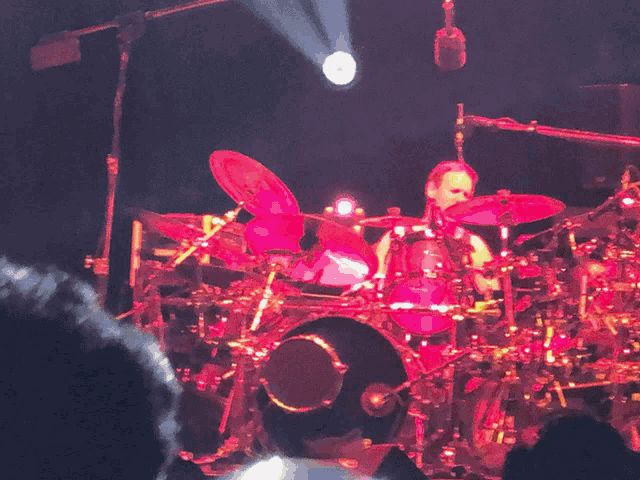 a man playing drums on a stage with a microphone hanging from the ceiling