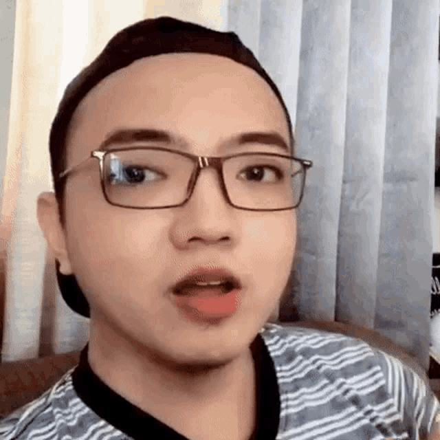 a young man wearing glasses and a baseball cap is sitting on a couch .