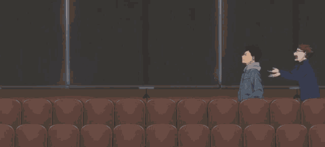 two men are standing in a row of brown seats in an auditorium .