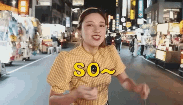 a woman in a yellow plaid shirt is walking down a street with the word so written on it