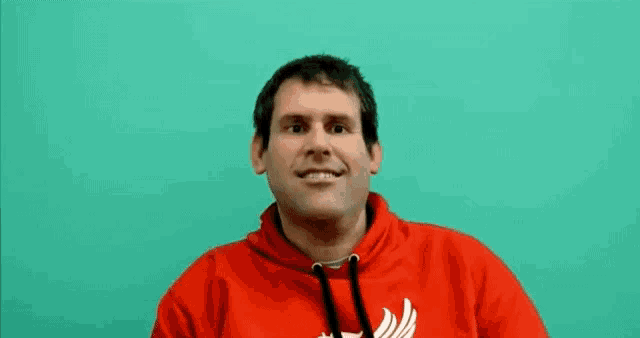 a man wearing a red hoodie is smiling and making a funny face .