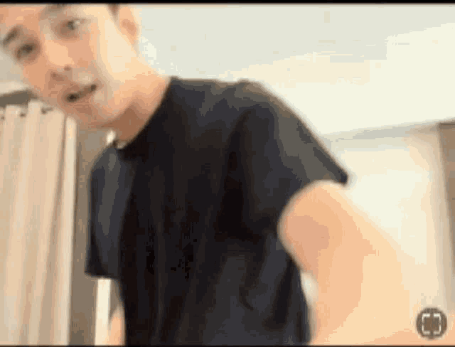a man in a black shirt is standing in front of a window in a room .