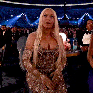 a woman in a gold dress sits in front of a crowd with a bottle of aquafina water