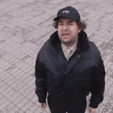 a man wearing a hat and a jacket is standing on a sidewalk